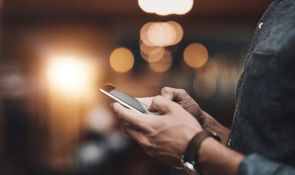 A man holding a mobile phone with lighted, blurred background